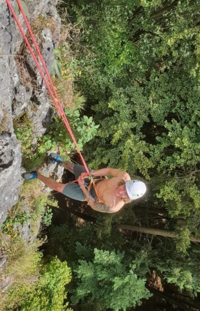 Sportler beim Klettern in einer Felswand im Wald; Symbol für funktionelles Krafttraining, mentale Stärke und leistungssteigernde Sporternährung.