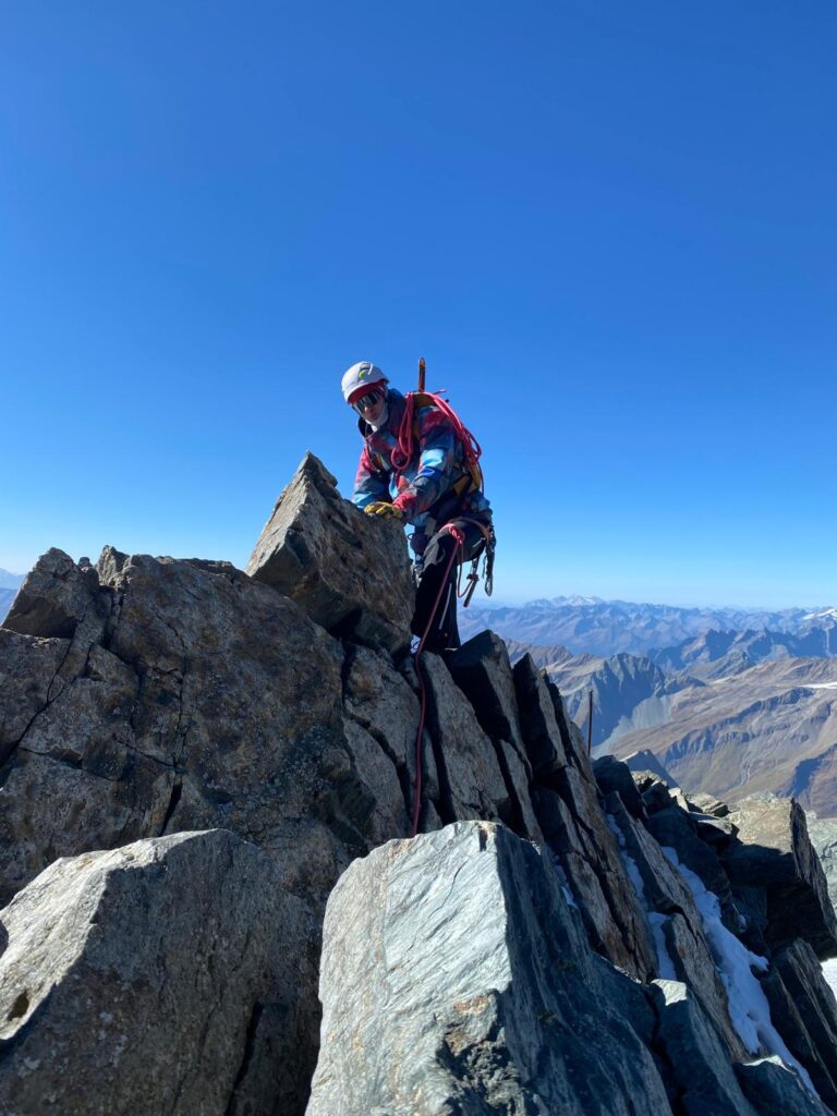 Bergsteiger in voller Ausrüstung auf einem Alpengipfel, Fokus auf Ernährung für extreme Ausdauerleistung. Performance.
